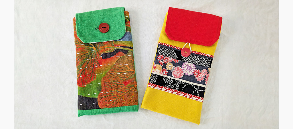 Deux sacs à bandoulière. Le premier est dans les tons vert et orange, le second est jaune avec un rabat rouge et des motifs à fleurs rouges, noirs et blancs.