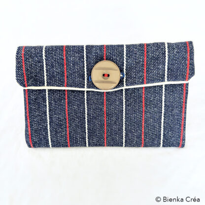 Vue de face de la pochette fermée par un bouton beige en jean à rayures rouge et blanche.
