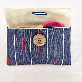 Vue de face de la pochette ouverte en jean à rayures rouge et blanche remplie de petits objets.