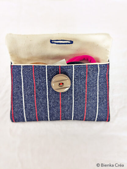 Vue de face de la pochette ouverte en jean à rayures rouge et blanche remplie de petits objets.