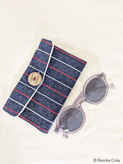 Vue du dessus de la pochette en jean à rayures rouges et blanches, avec ses lunettes.